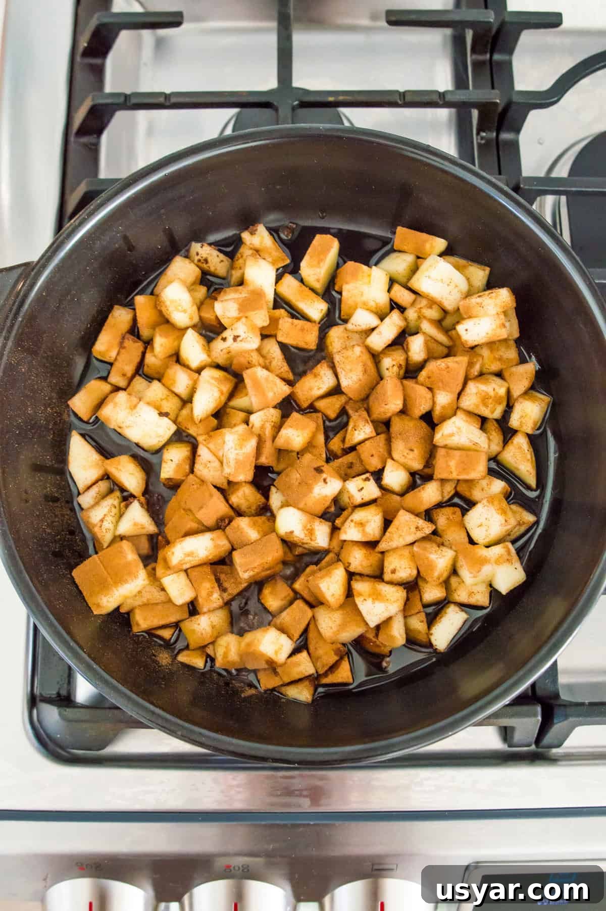 Gluten-Free Vegan and Paleo Apple Pie Bars 6 Apple pieces cooking in a black pan on a stovetop.