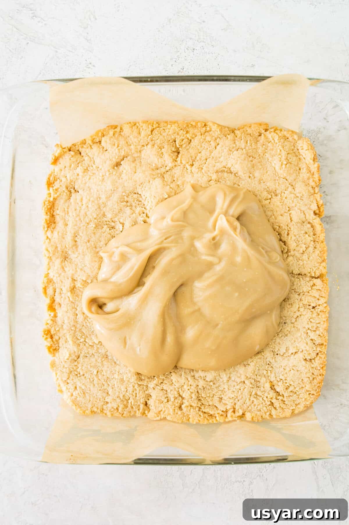 Gluten-Free Vegan and Paleo Apple Pie Bars 8 A shortbread crust in a square baking pan with caramel spread over it.