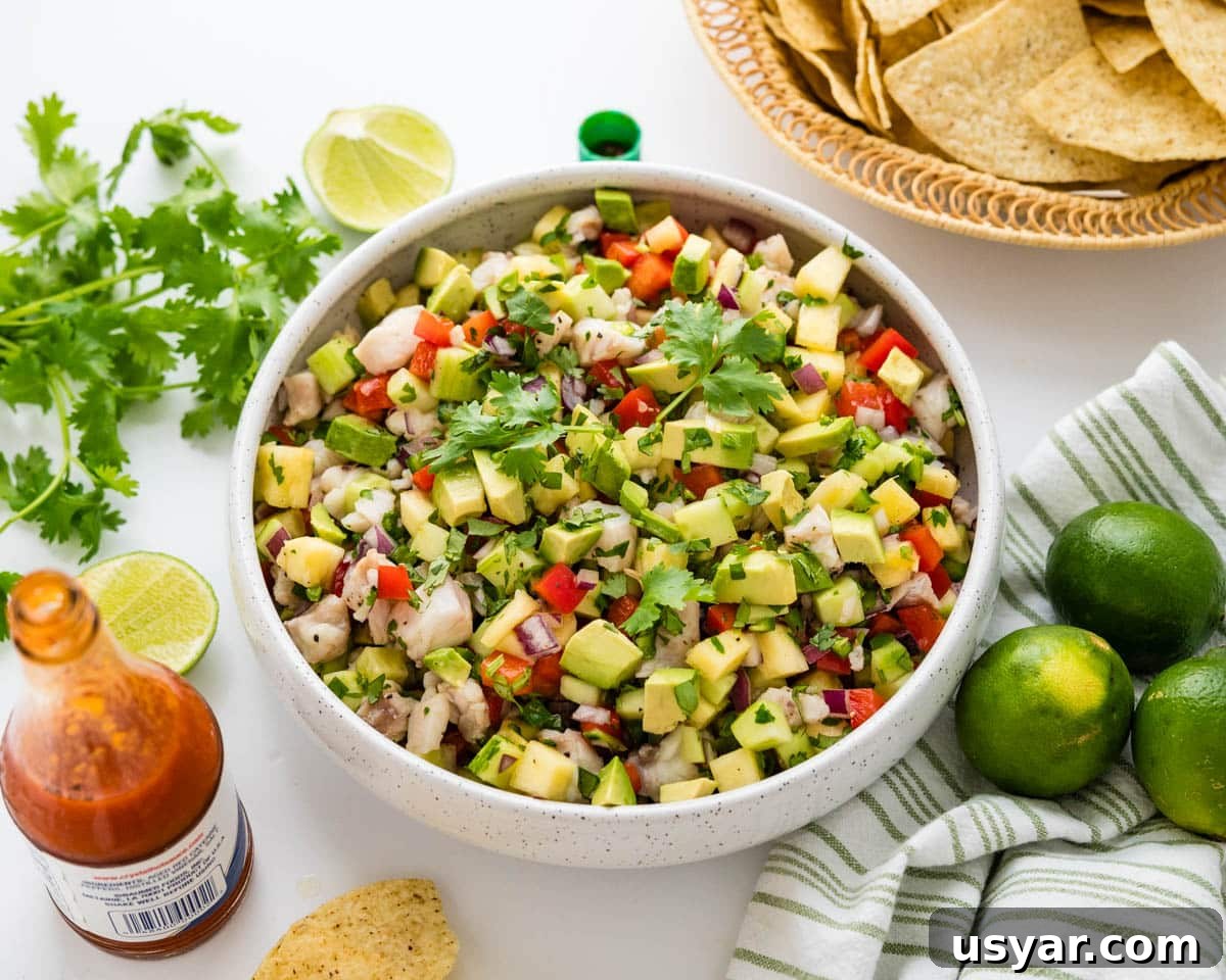 A bowl of fish ceviche with hot sauce, tortilla chips and limes.