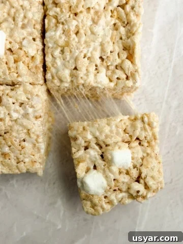 a close up of brown butter rice krispie treats with a marshmallow being pulled and stretched.