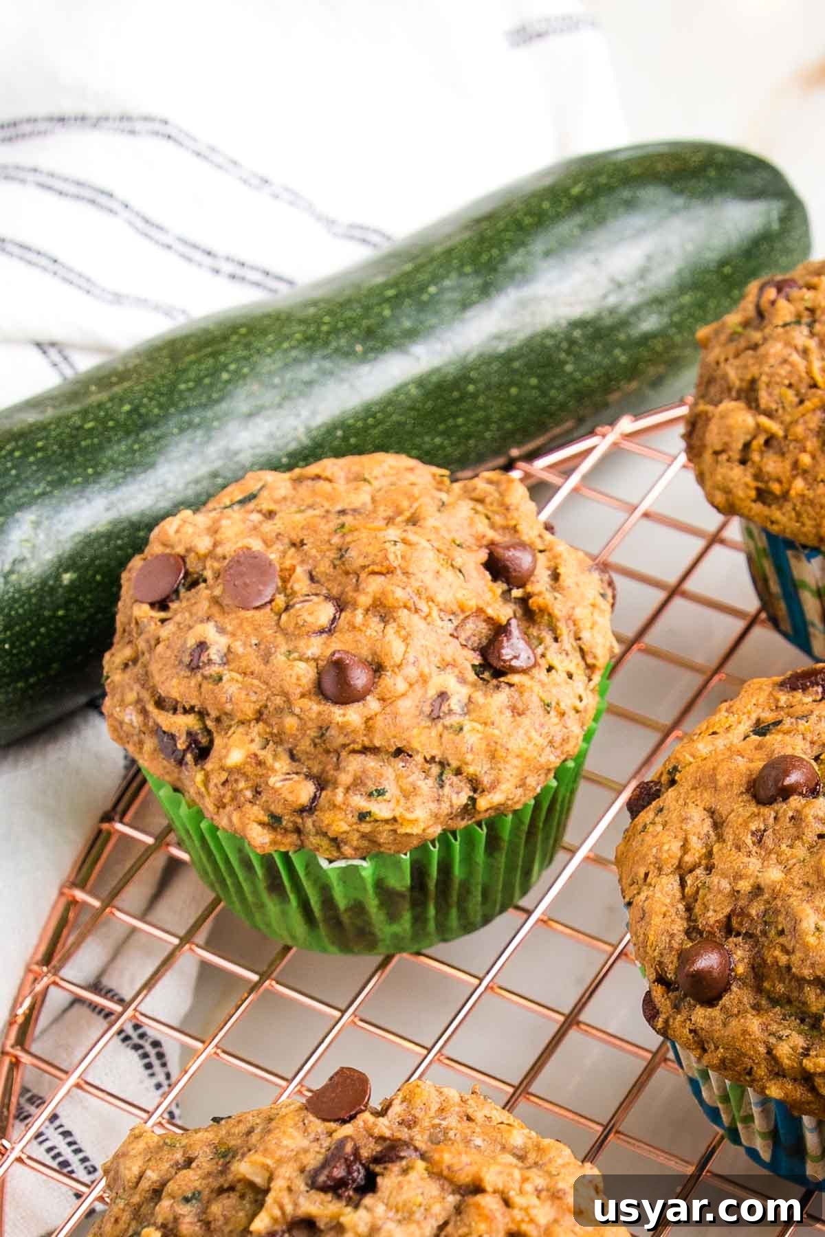 Chocolate chip zucchini muffin, cooling on a wire rack, with a large fresh zucchini in the background.