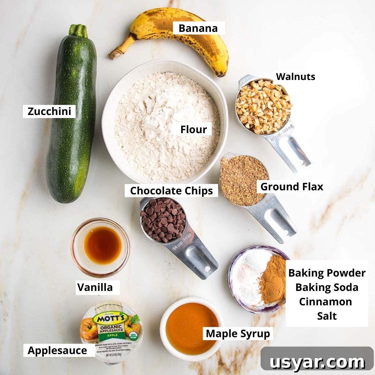 Labeled zucchini muffin ingredients: banana, zucchini, flour, walnuts, flaxseed, chocolate chips, vanilla, maple syrup, baking soda, baking powder, cinnamon. 