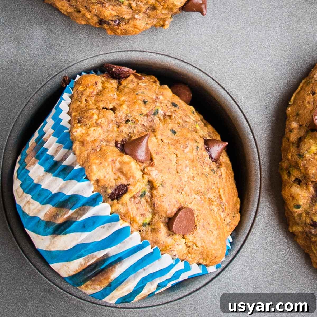 Chocolate Chip Zucchini Muffin inside the muffin tin, turned on its side so you can see the pretty striped blue wrapper.