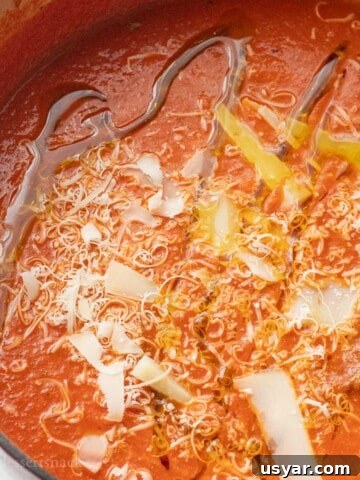 Red pot of homemade canned tomato soup with parmesan and olive oil drizzled on top.