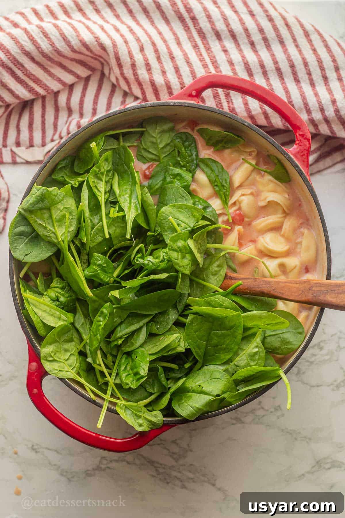 Tuscan Tortellini Soup with Tomatoes and White Beans 7 Spinach in soup pot with wooden spoon and tortellini.