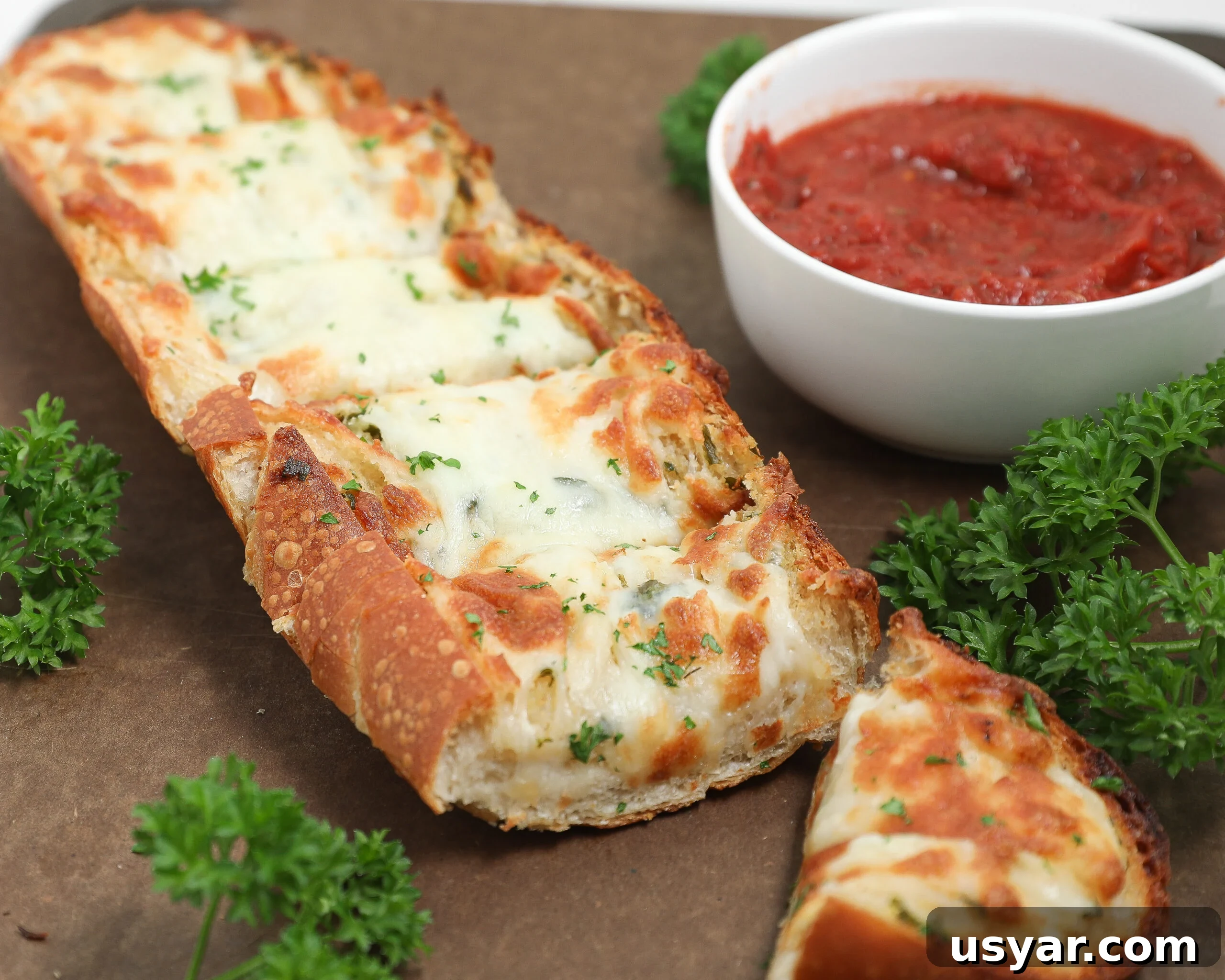 Cheesy garlic bread topped with melted mozzarella and parsley beside marinara sauce