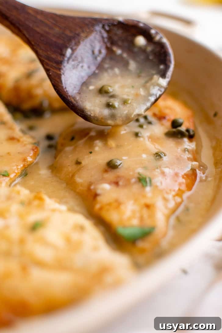 Lemon caper sauce being spoon over a chicken breast.