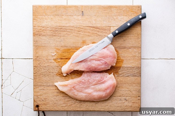 Chicken breast being cut in half lengthwise.