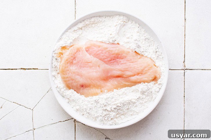 Chicken being dredged in seasoned flour.