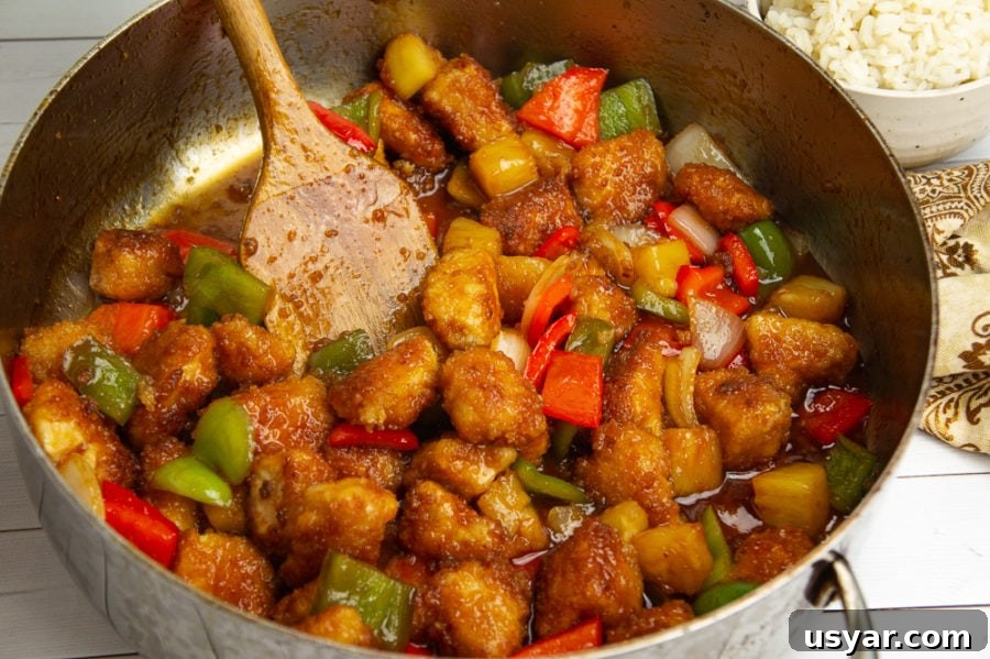 homemade sweet and sour chicken with pineapples and peppers in a large saute pan with a spoon