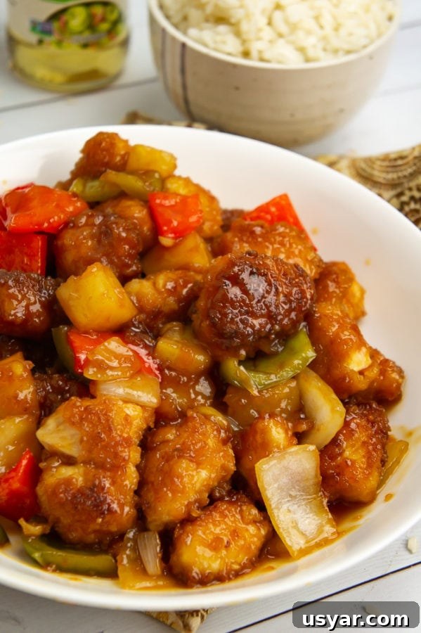 a large white bowl of sweet and sour chicken with a small bowl of rice behind it.