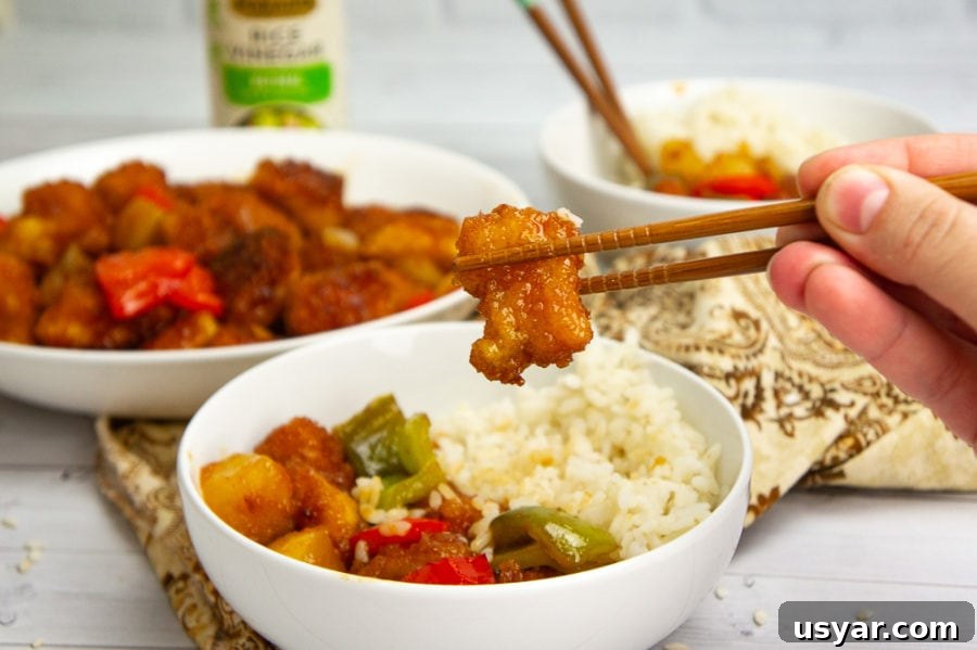 a bowl of sweet and sour chicken with rice and chopsticks picking up a piece of chicken