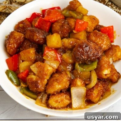 a large white bowl of sweet and sour chicken with pineapple and peppers