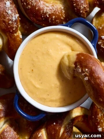An overhead shot of Beer Cheese in a small bowl on a platter with soft pretzels.