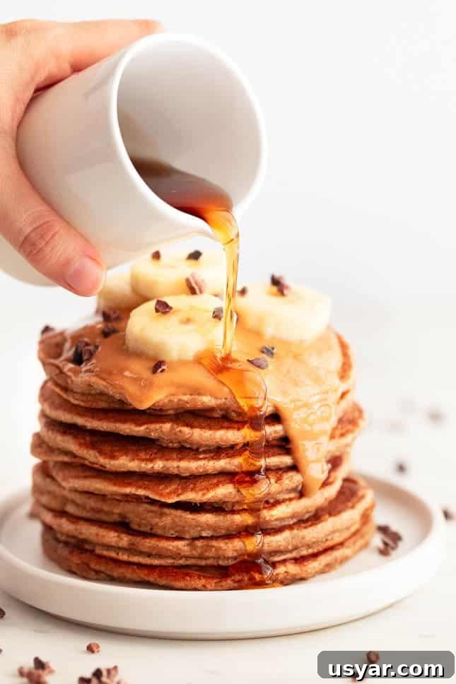 Fluffy Vegan Banana Pancakes Recipe with Maple Syrup 2 Stack of vegan banana pancakes topped with peanut butter, chocolate chips, banana, and syrup.