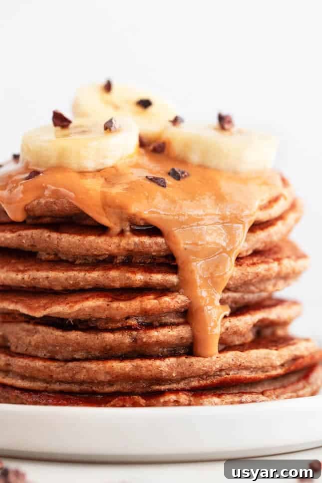 Fluffy Vegan Banana Pancakes Recipe with Maple Syrup 4 Vegan banana pancakes stack with peanut butter, chocolate chips, and sliced banana.