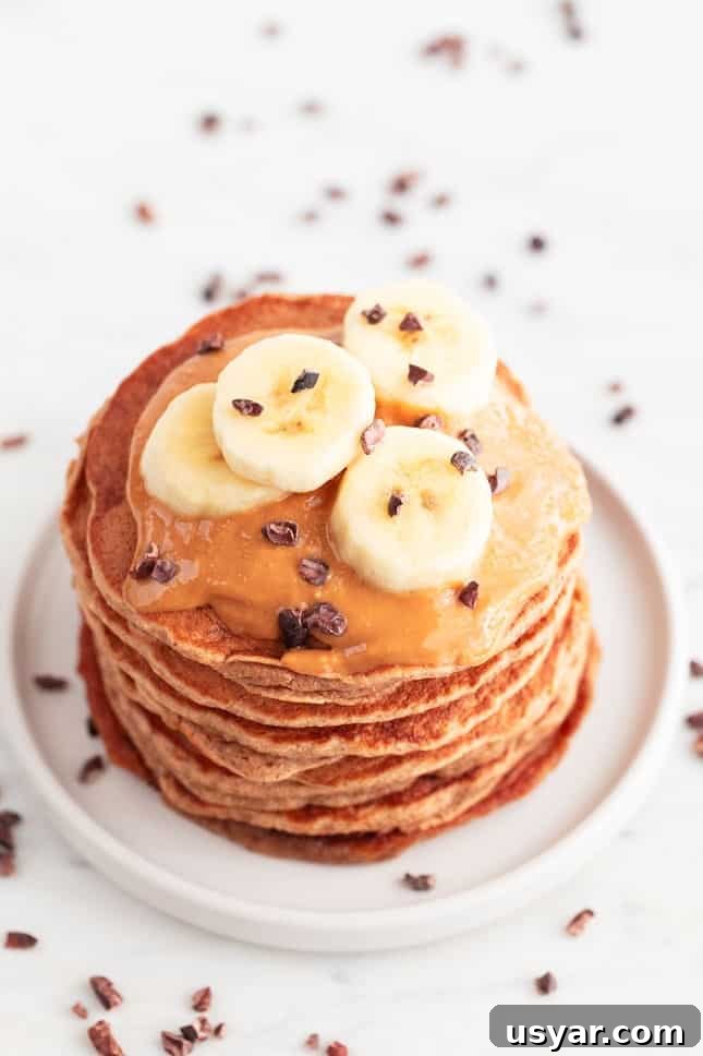 Fluffy Vegan Banana Pancakes Recipe with Maple Syrup 5 Vegan banana pancakes stacked with peanut butter, chocolate chips, and banana slices.