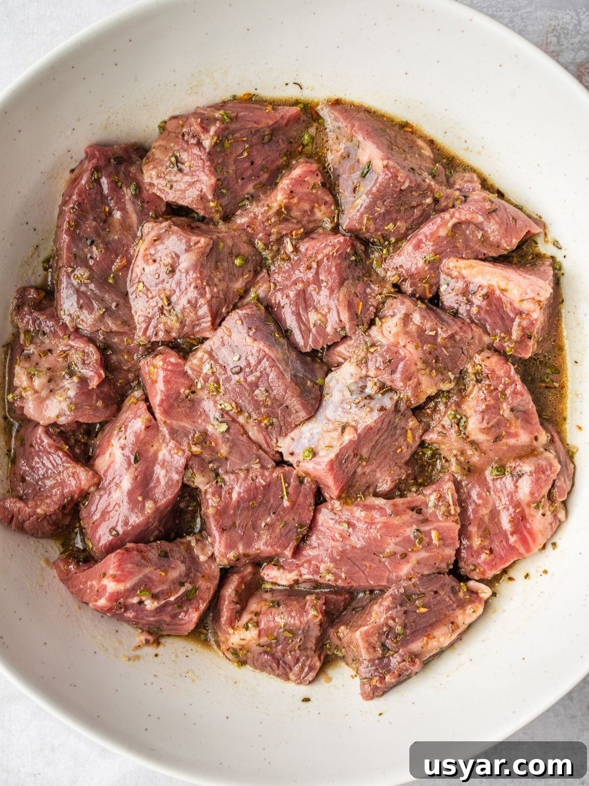 Authentic Middle Eastern Beef Shish Kebab Recipe with Sides 6 Chunks of raw beef marinating in a white bowl, coated with herbs and spices.
