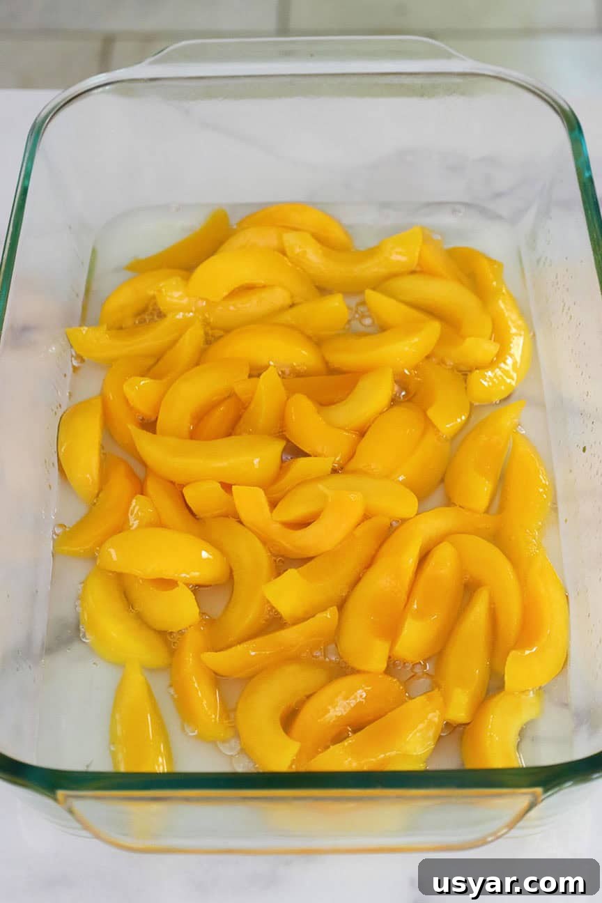 Cake Mix Peach Cobbler with Canned Peaches 4 A 9 by 13 inch glass baking dish with sliced peaches in syrup.