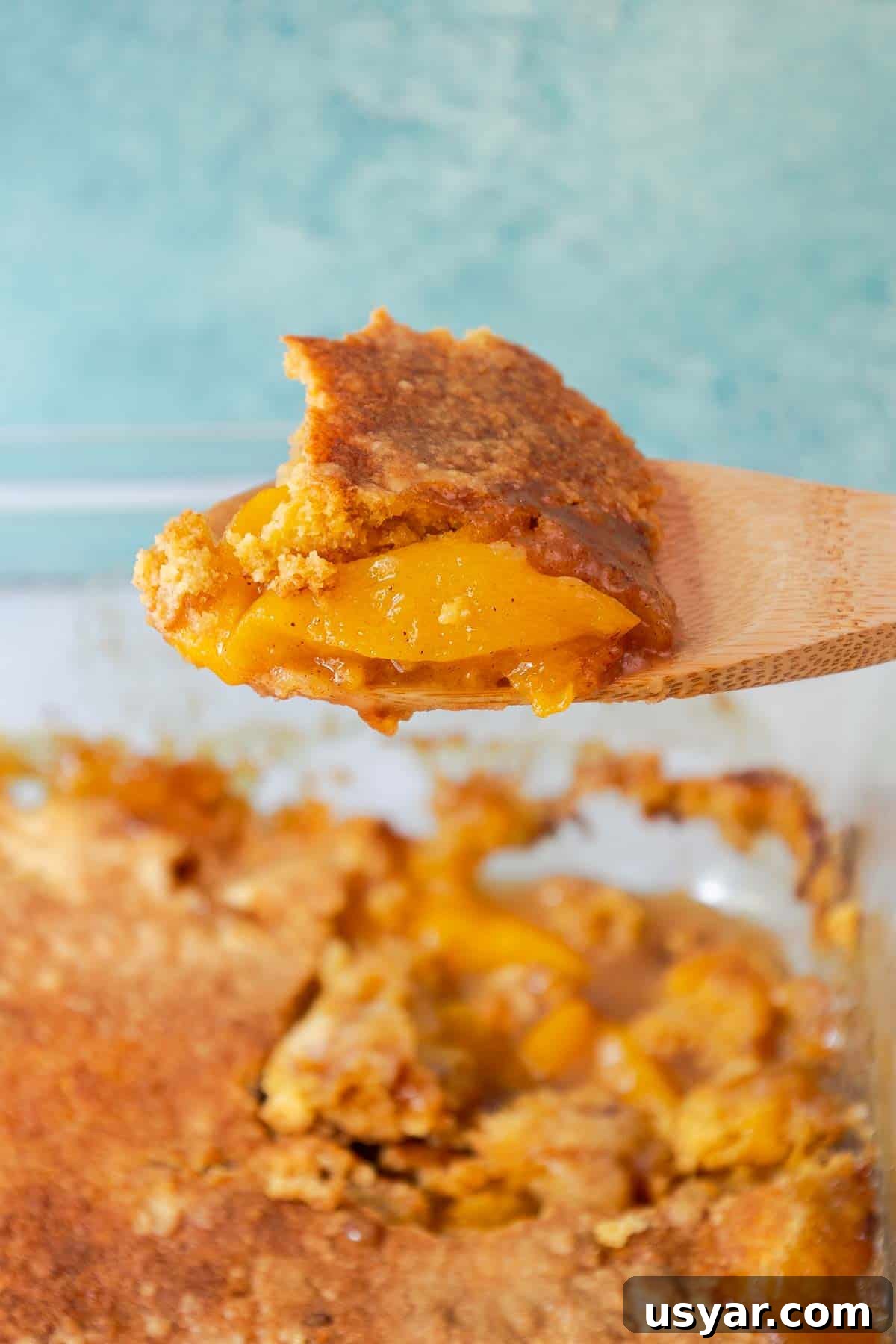 Cake Mix Peach Cobbler with Canned Peaches 10 A wooden spoon holding a scoop of peach cobbler.