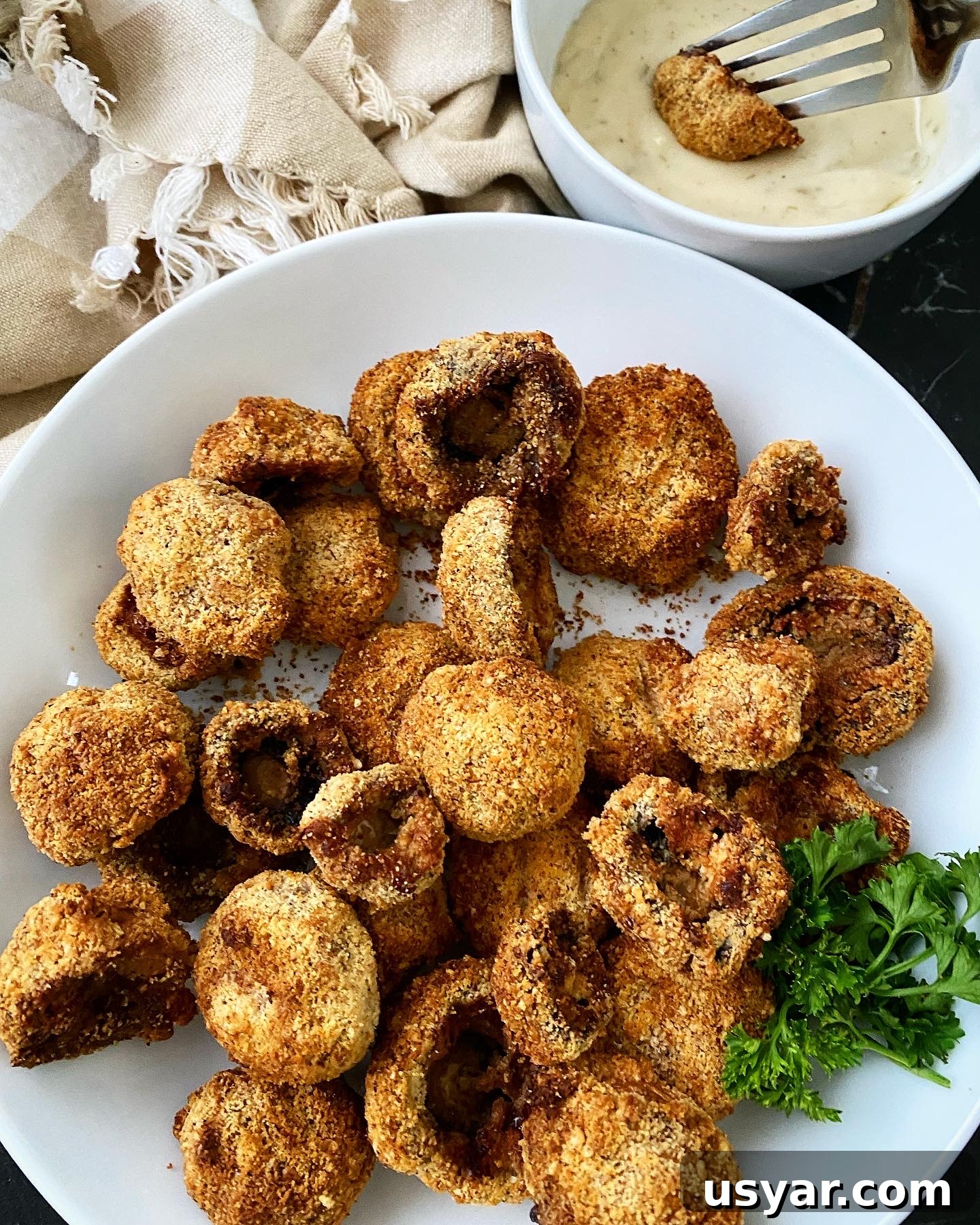 cooked air fryer fried mushrooms on a white plate with a mushroom dipped in ranch