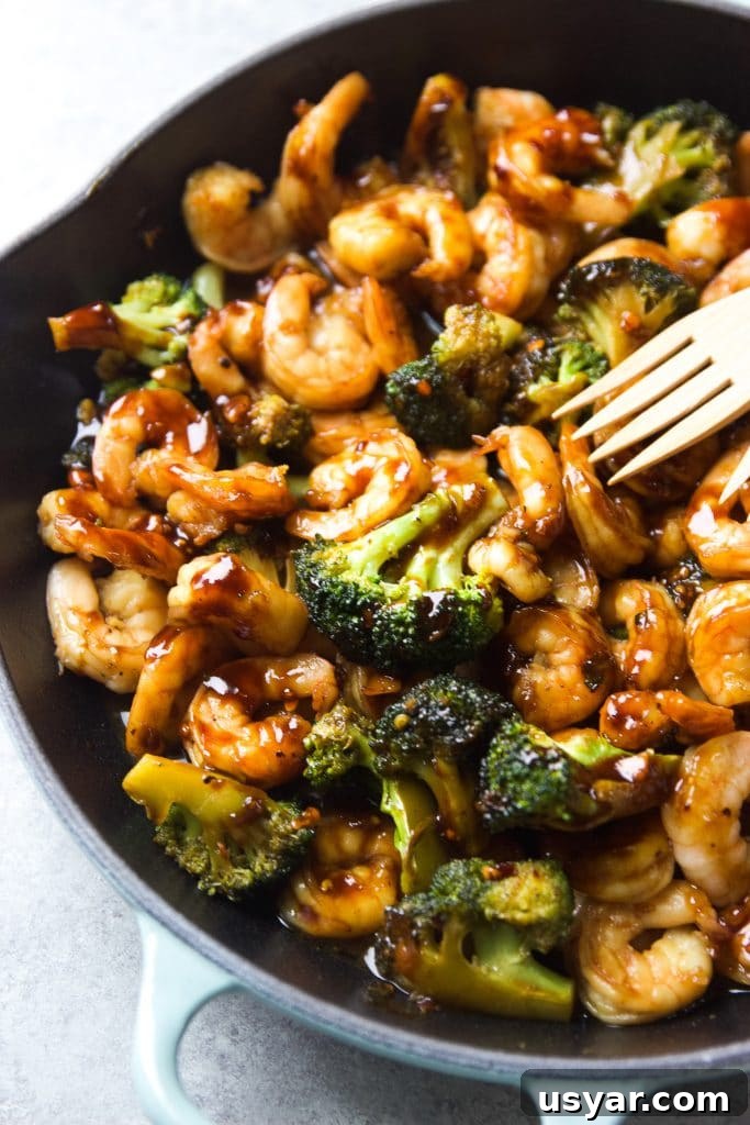 shrimp stir fry with broccoli served in a light blue Le Creuset cast iron skillet, with two wooden spoons
