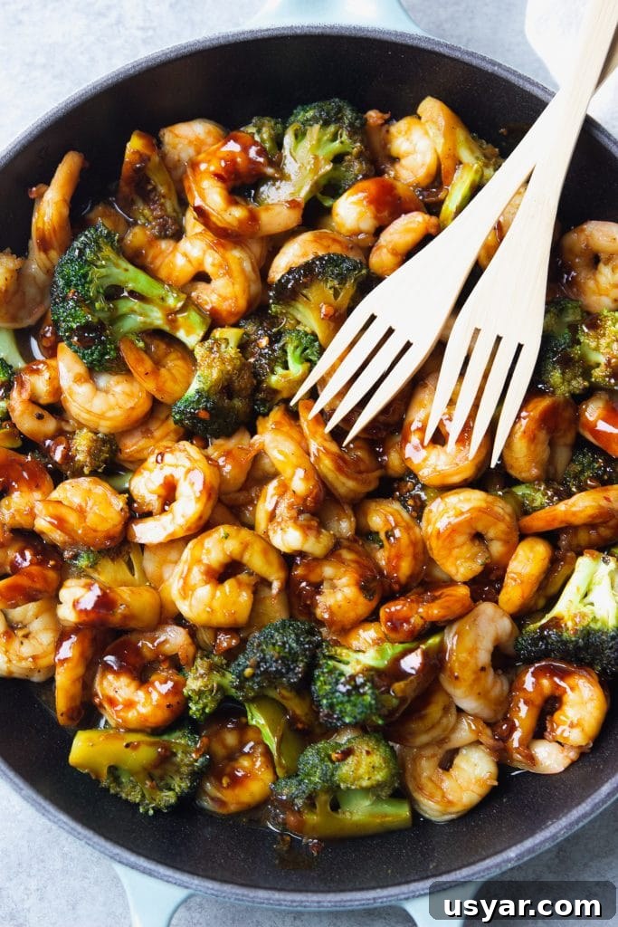 shrimp stir fry with broccoli served in a light blue Le Creuset cast iron skillet, with two wooden spoons.