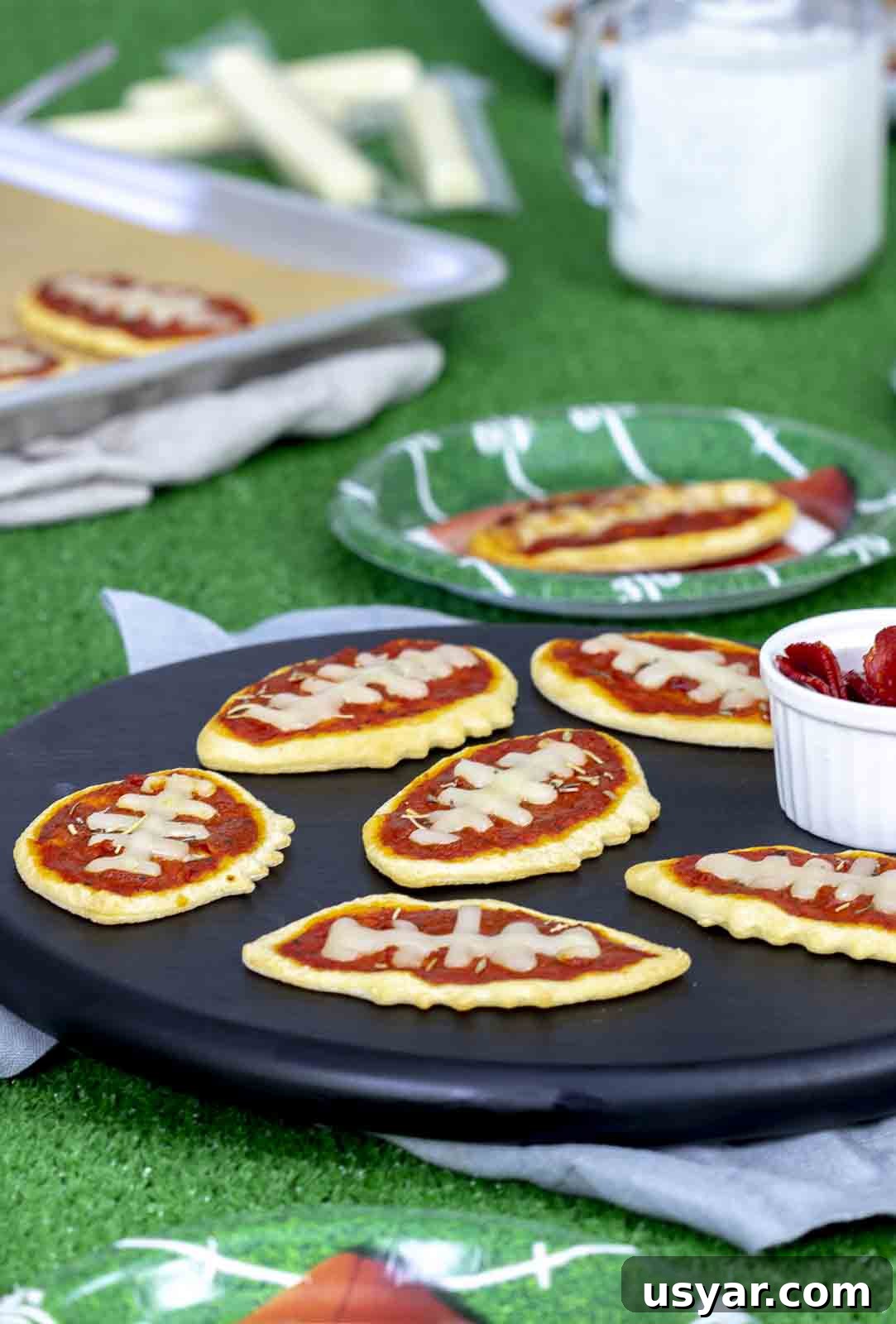 Game Day Mini Football Pizzas with Crescent Roll Dough 2 Mini pizza footballs on cutting board with football backdrop.
