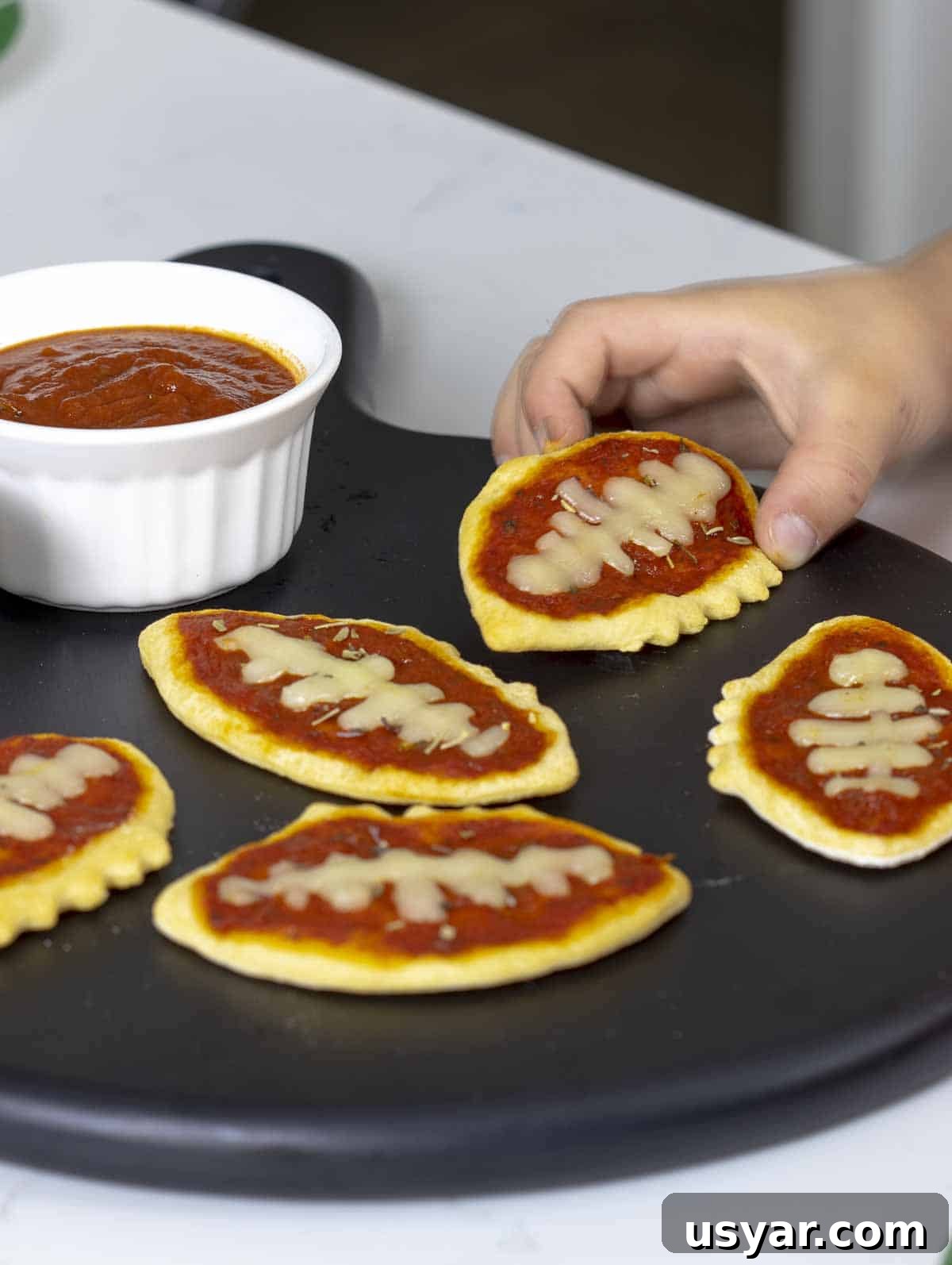 Game Day Mini Football Pizzas with Crescent Roll Dough 6 Hand grabbing small pizzas.