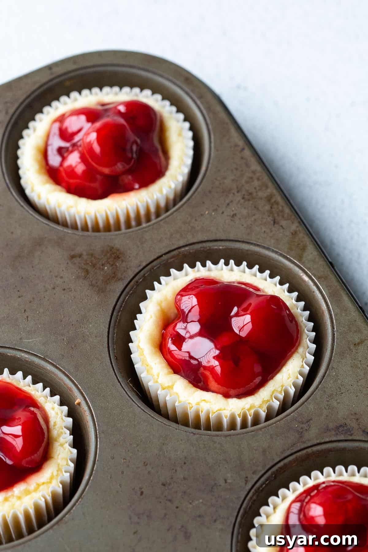 Mini Cherry Cheesecakes with Graham Cracker Crust 7 mini cherry cheesecakes in a muffin tin.