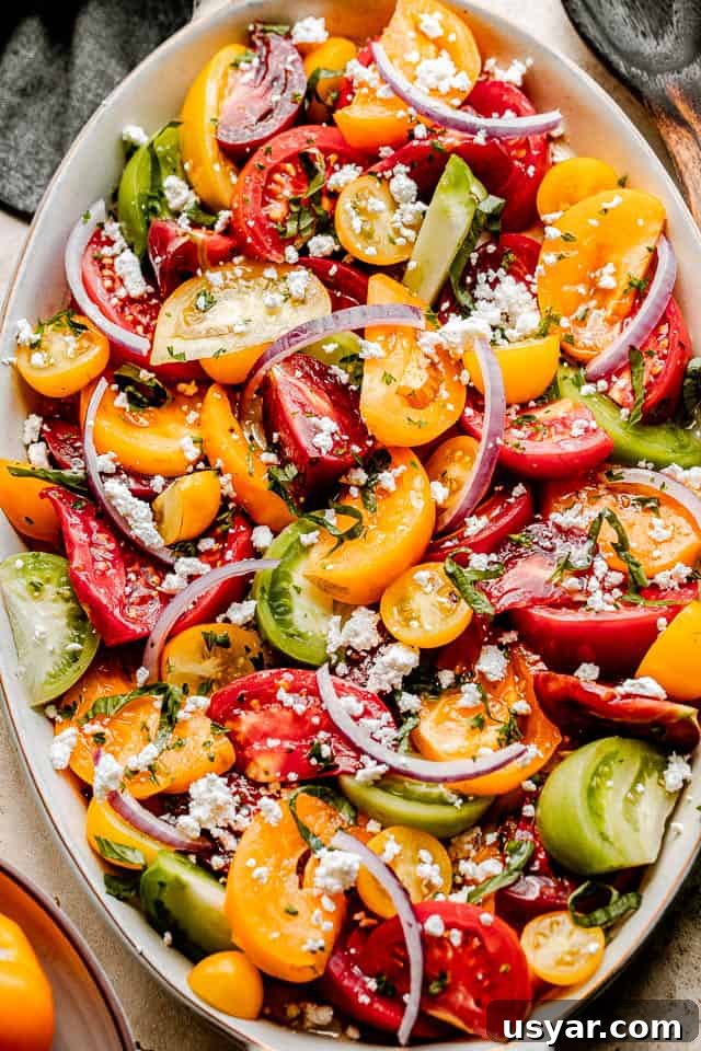 Heirloom Tomato Salad with Basil Vinaigrette 2 top shot of wedges of heirloom tomatoes in an oblong salad bowl topped with slices of red onions and crumbled feta cheese