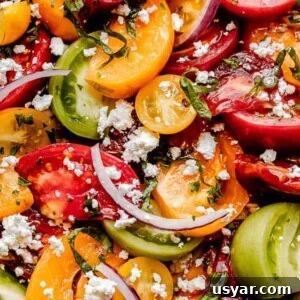 close up shot of wedges of colored tomatoes topped with slices of red onions and crumbled feta cheese
