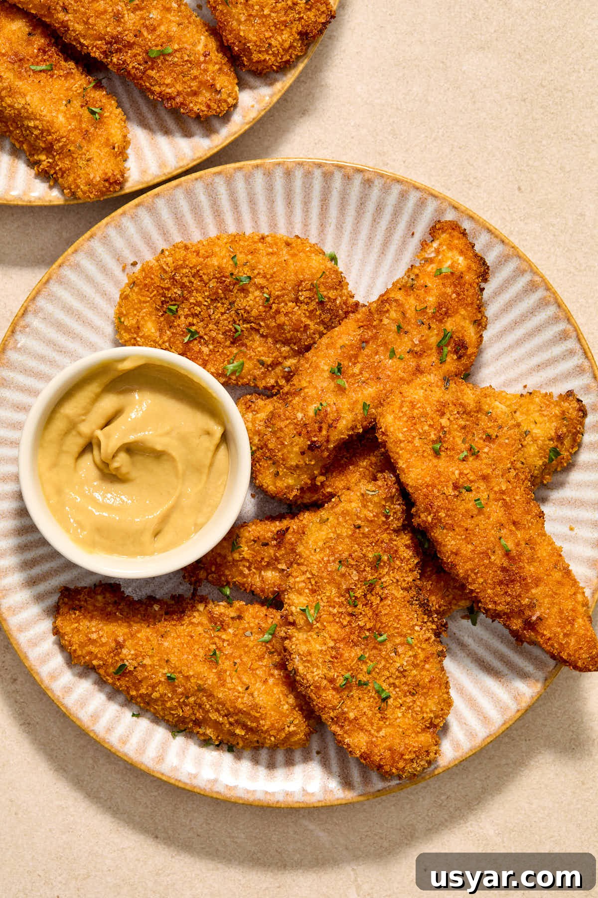 Chicken strips served on a plate with honey mustard on the side for dipping.