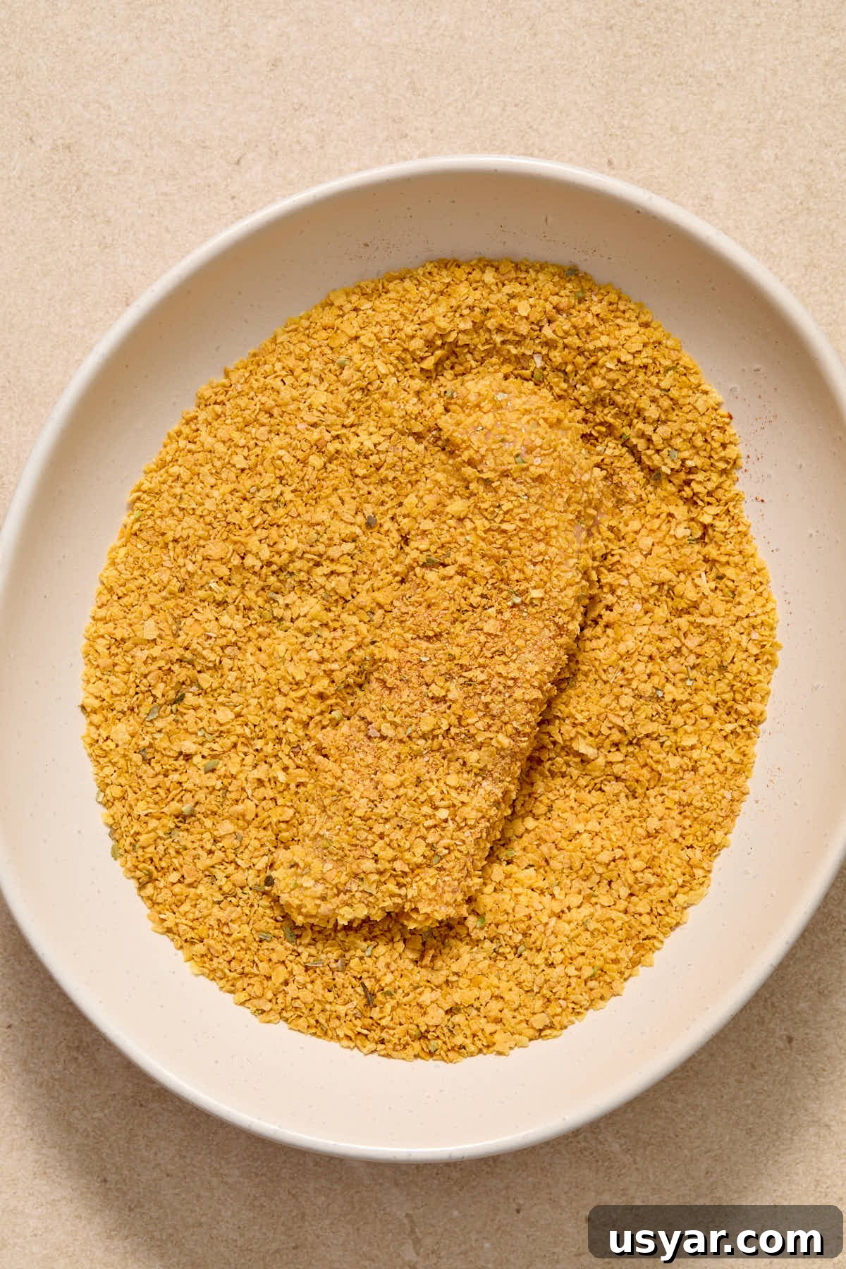 A chicken strip being coated in the cornflake crumb mixture.