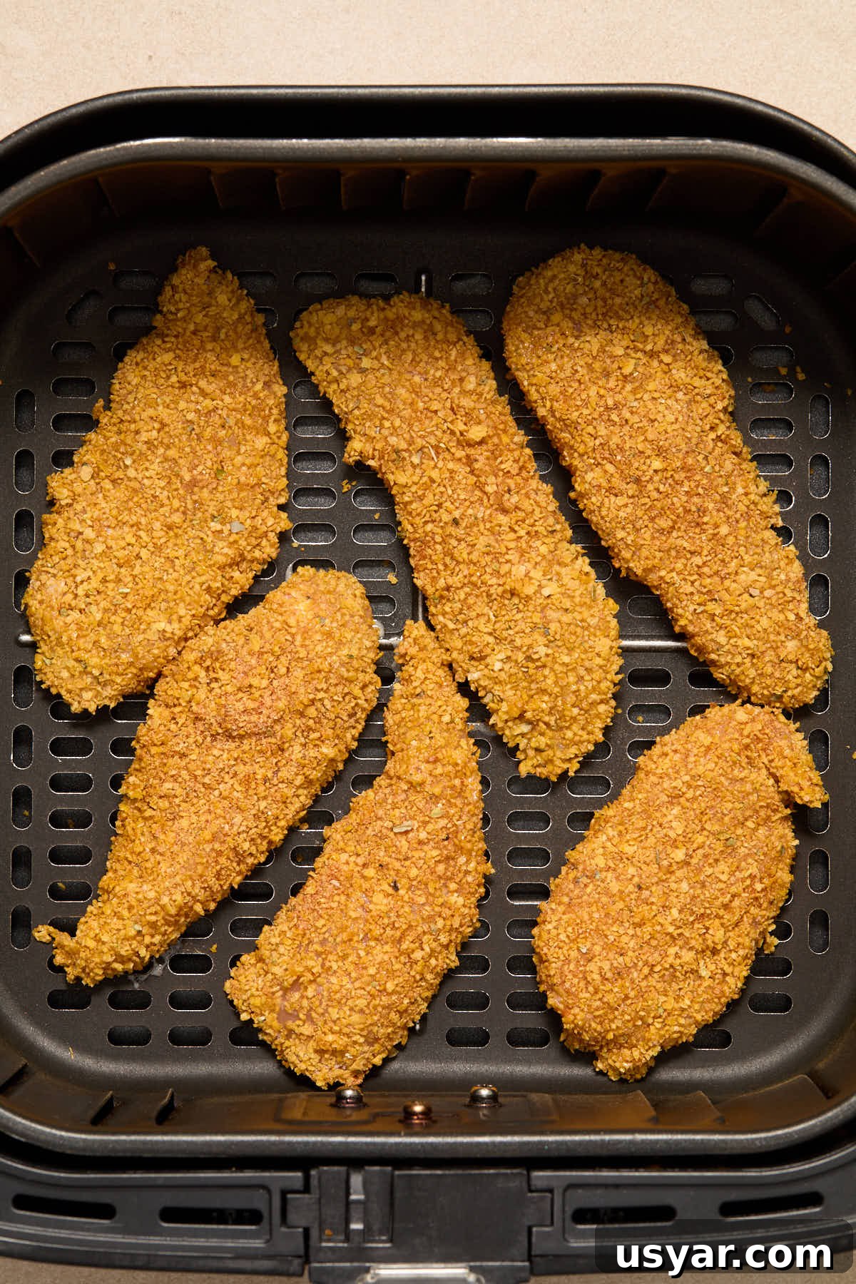 Cornflake crusted chicken strips arranged in a single layer in the air fryer basket.