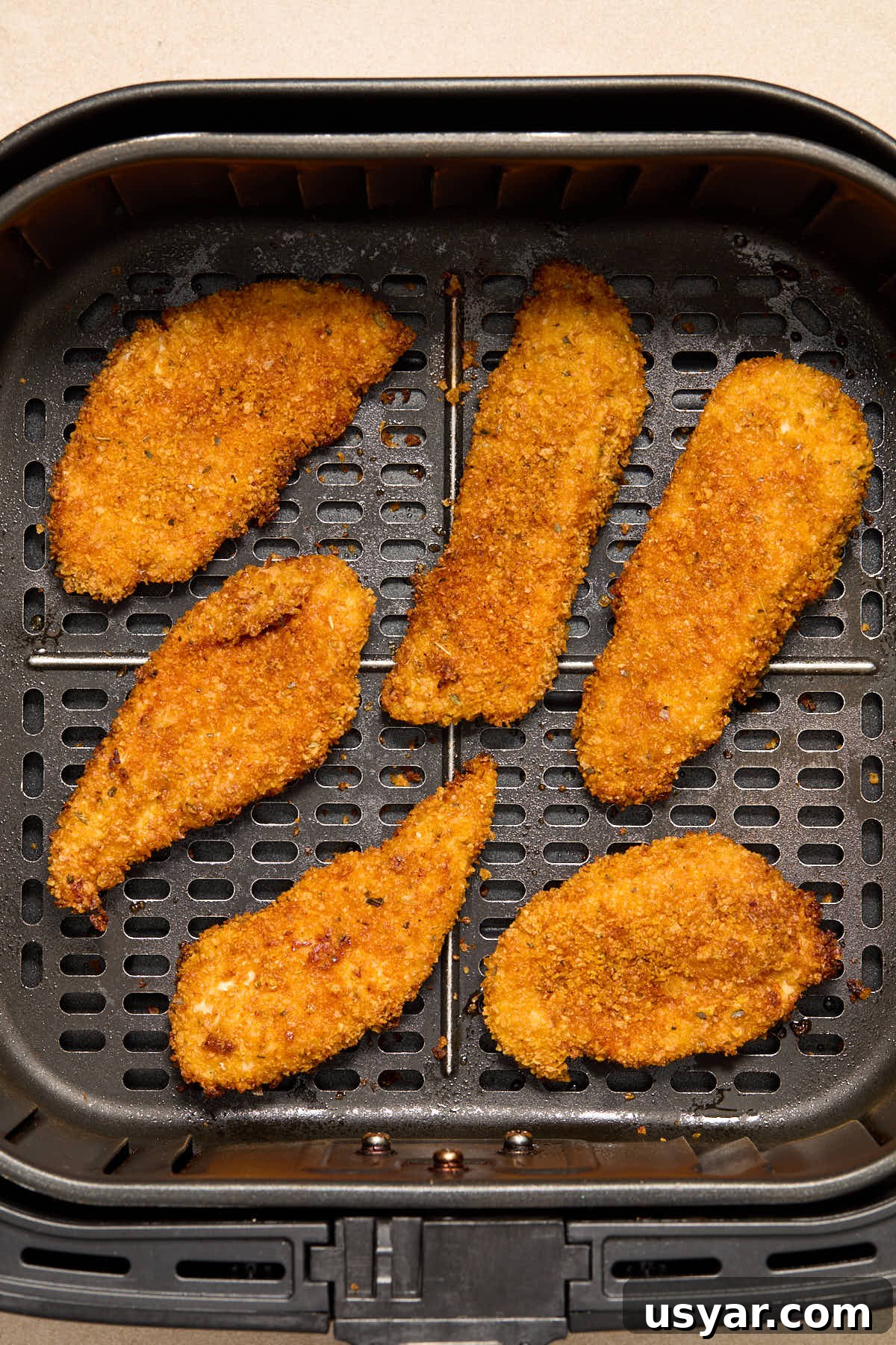 Air fried chicken strips in the air fryer basket.