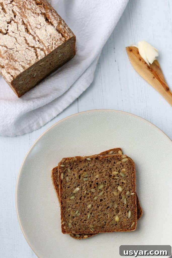 Danish Sourdough Rye Bread Rugbrød Recipe 2 Rye bread slices on a plate next to a loaf of rye bread and a wooden knife with butter