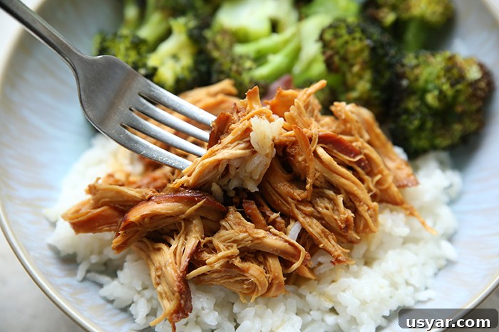 Slow Cooker Honey Garlic Chicken Recipe 3 Shredded garlic honey chicken served over rice with a fork inserted diagonally on the left and a serving of steamed broccoli all on a plate.