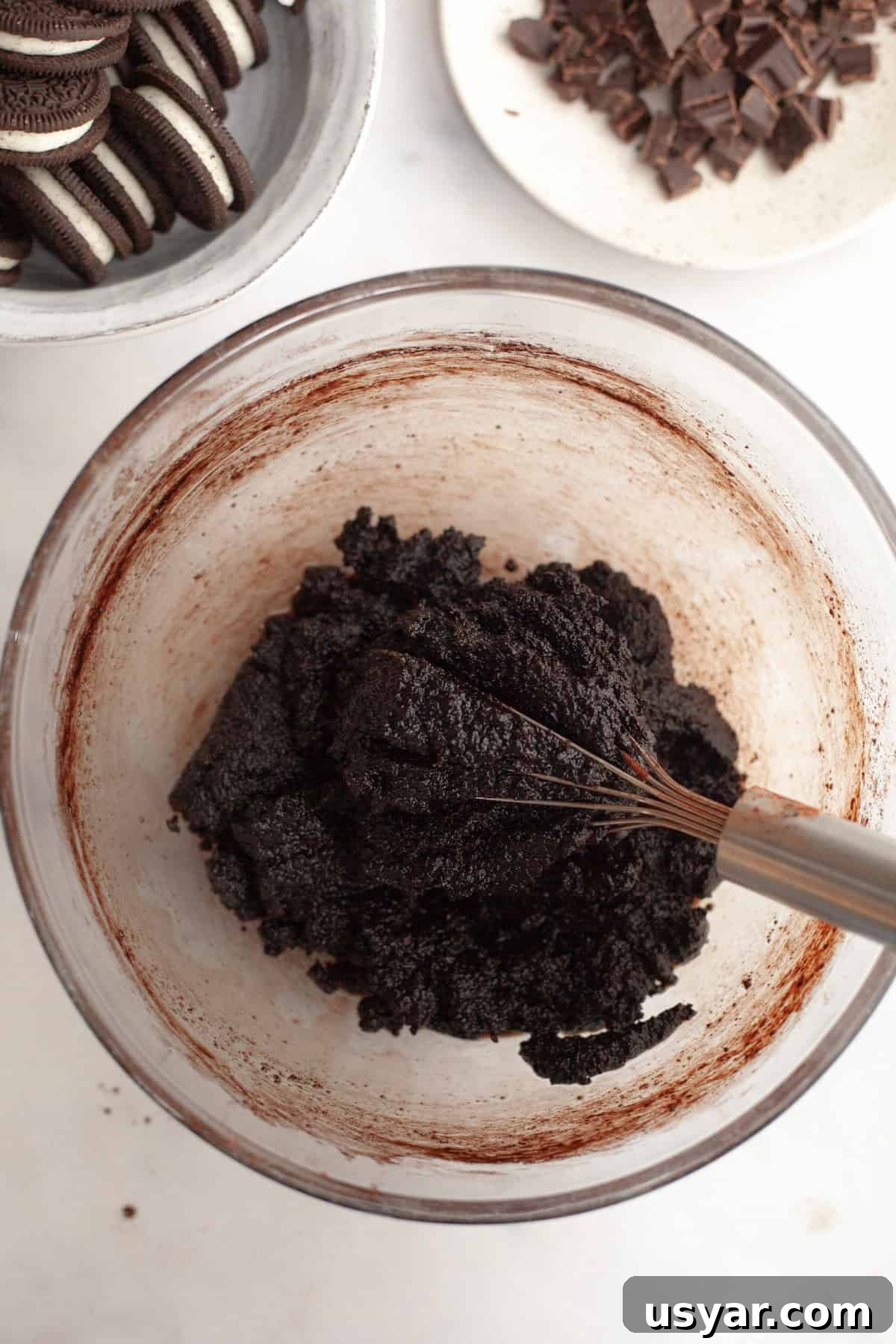 A glass bowl with a whisk and brownie batter.
