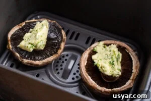Two Portobello mushrooms with garlic butter on top in an air fryer tray