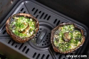 Two cooked Portobello mushrooms with melted garlic butter inside the mushroom in an air fryer basket