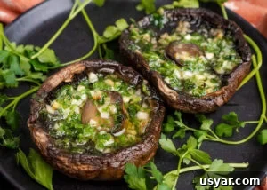 Two cooked Portobello mushrooms with melted garlic butter inside the mushroom served on a black plate with fresh parsley around them