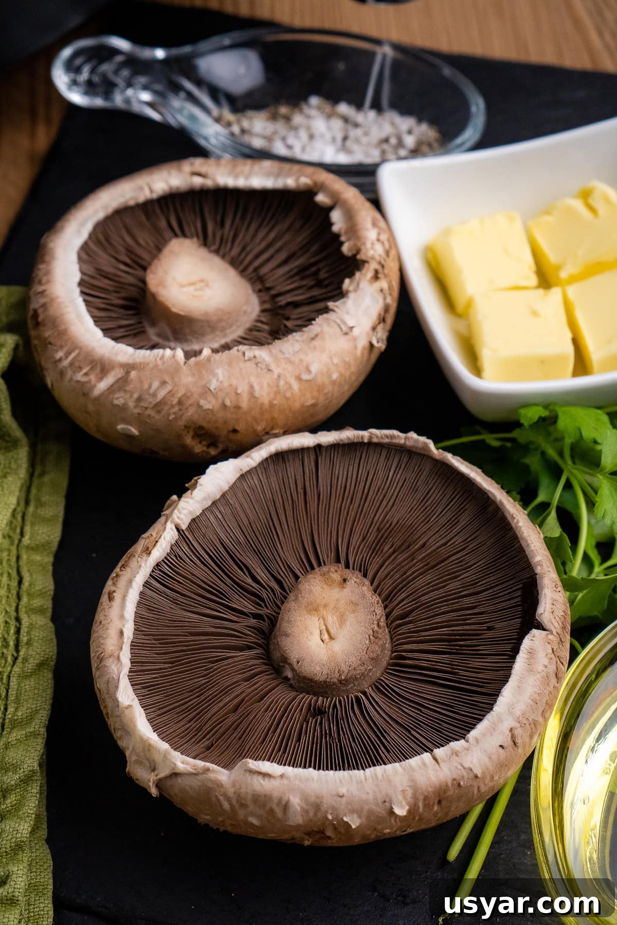 Two large flat mushrooms known as Portobello mushrooms on black slate