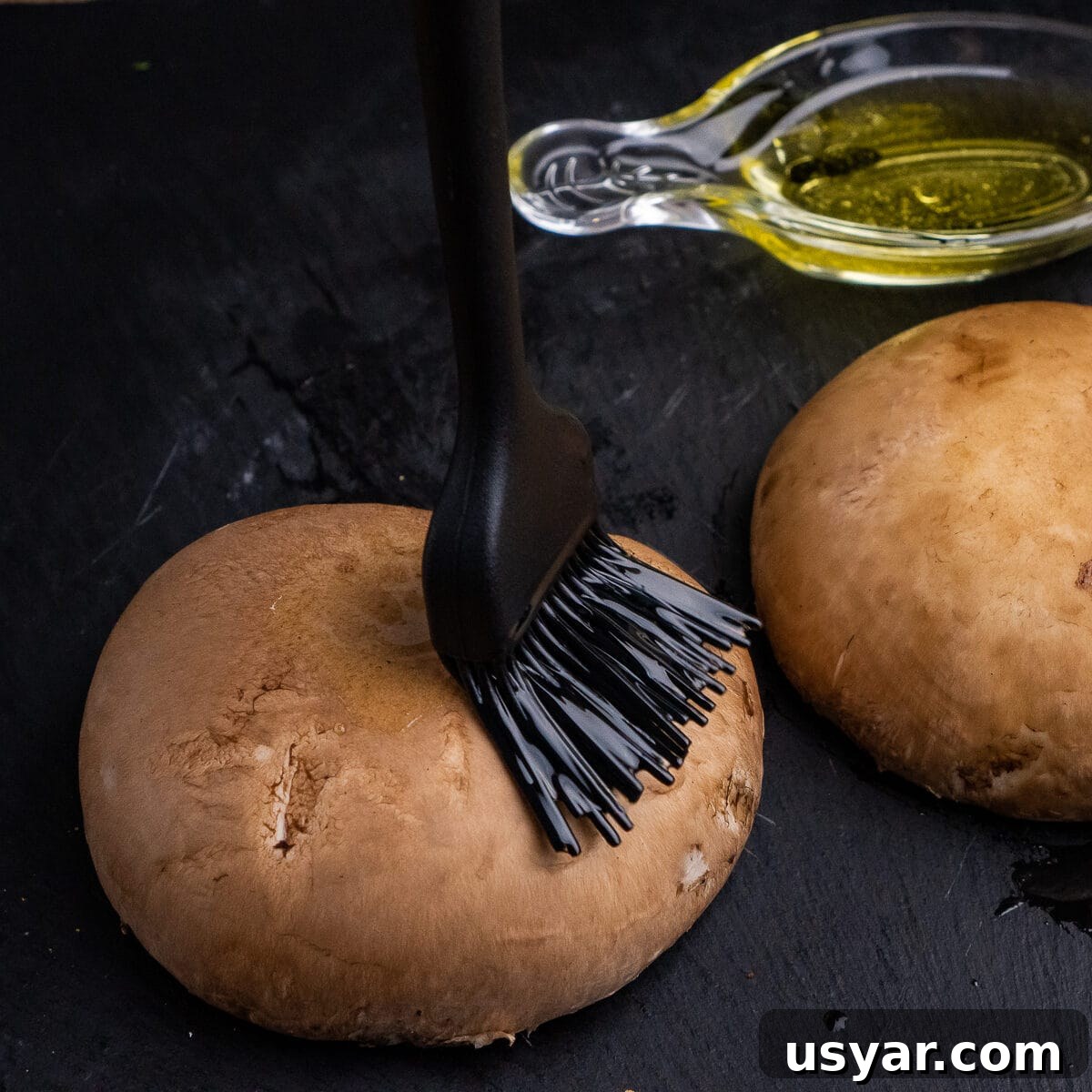 Spreading olive oil over two mushrooms using a pastry brush
