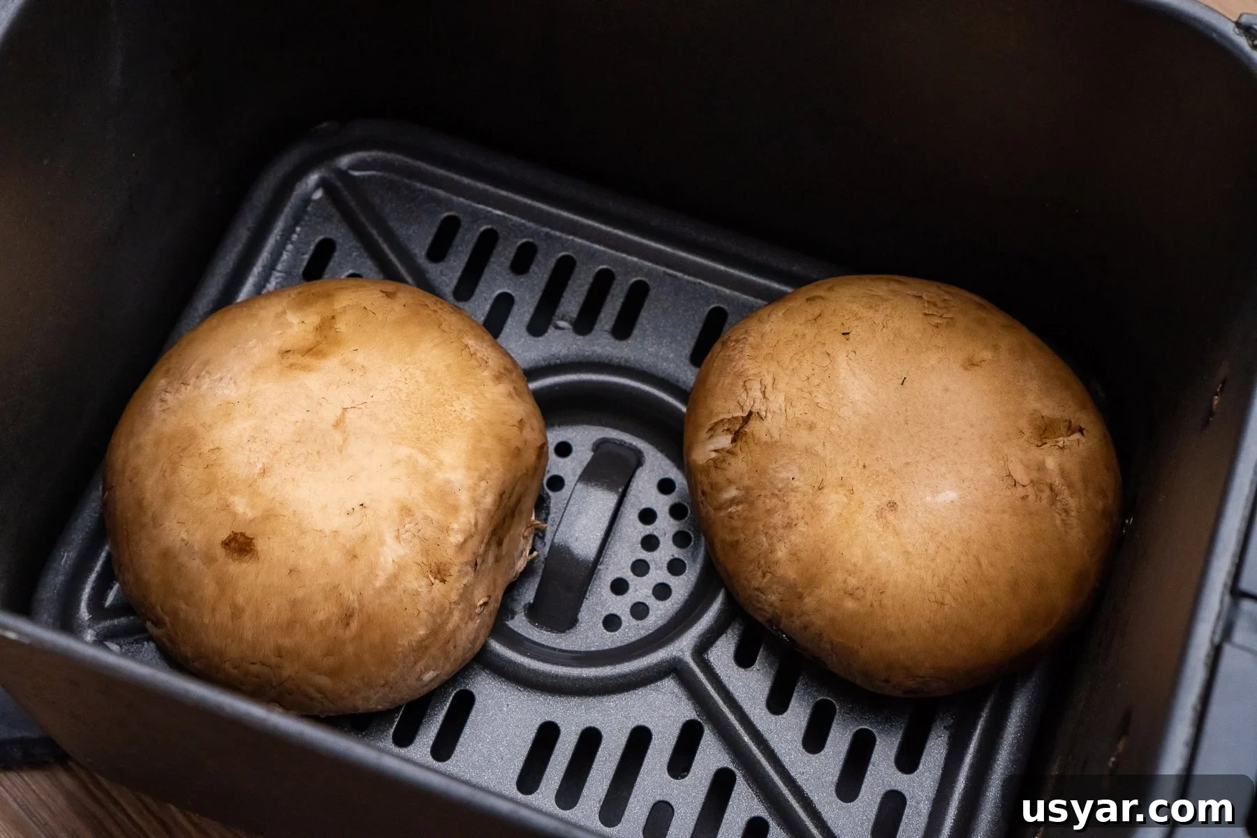 Two large mushrooms in an air fryer tray
