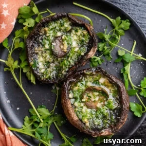 Two cooked Portobello mushrooms with melted garlic butter inside the mushroom served on a black plate with fresh parsley around them and sea salt sprinkled over the top