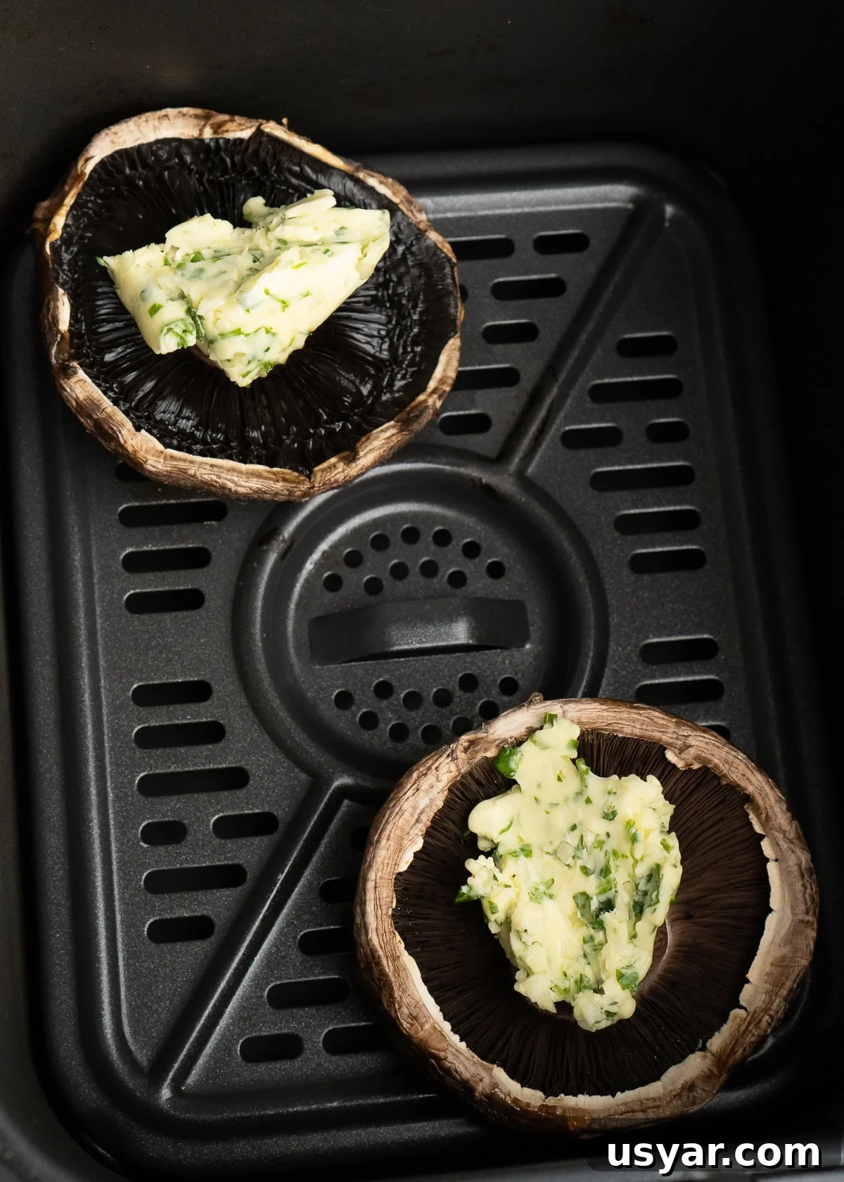 Two Portobello mushrooms with garlic butter on top in an air fryer basket