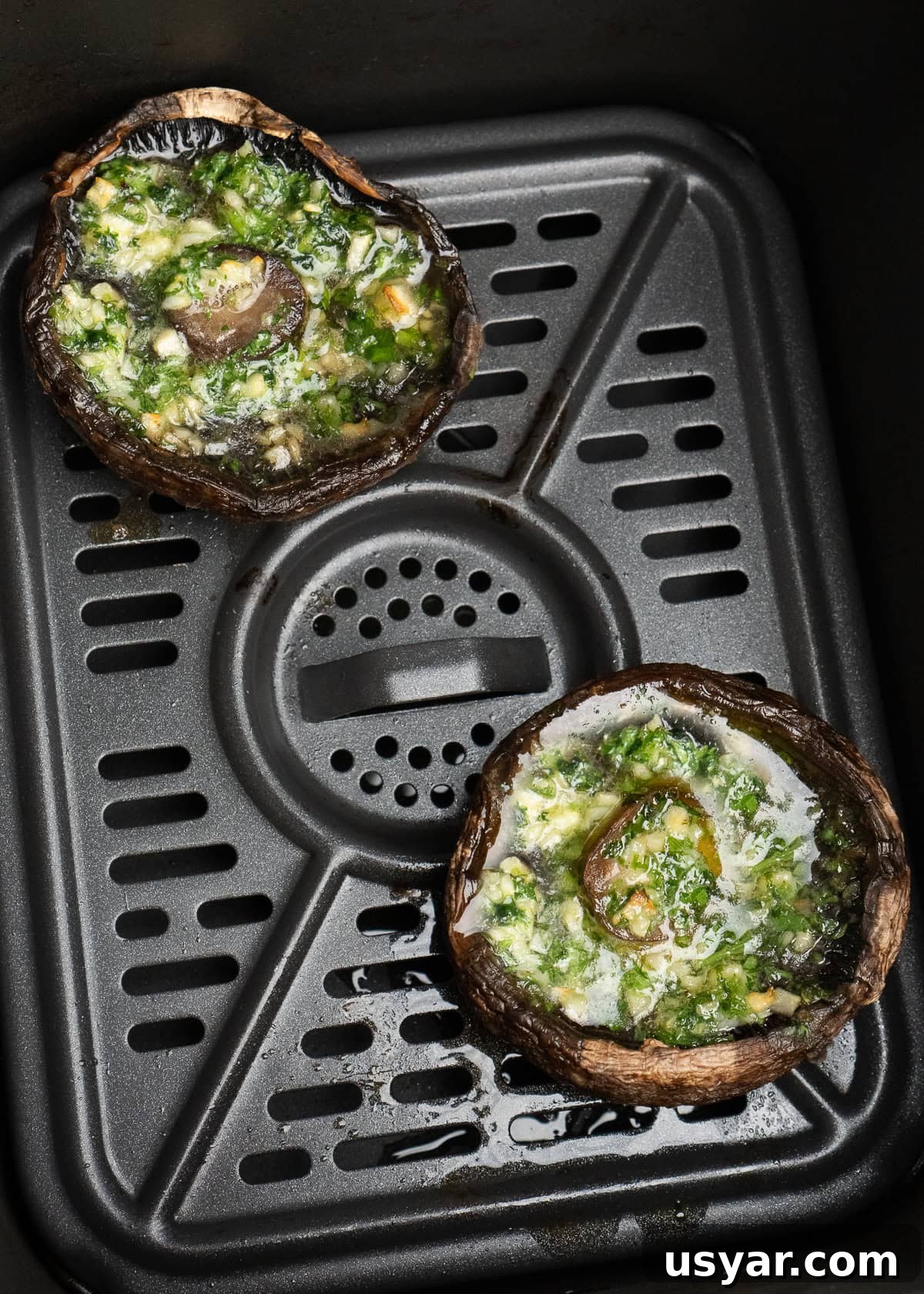 Two cooked air fried mushrooms with melted garlic butter inside the mushroom in an air fryer tray