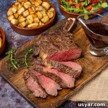 Medium rare bone in rib eye steak sliced on a wooden chopping board served with paramentier potatoes, salad and red wine jus