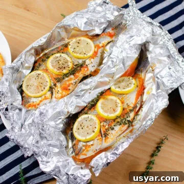 Two Sea bream cooked with lemon slices and sprigs of thyme on top unwrapped in aluminum foil